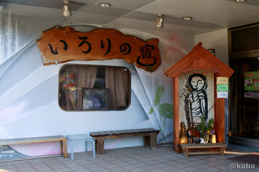 入口横にある、木製の大きな看板とお地蔵様。壁沿いには休憩用の木製のベンチ