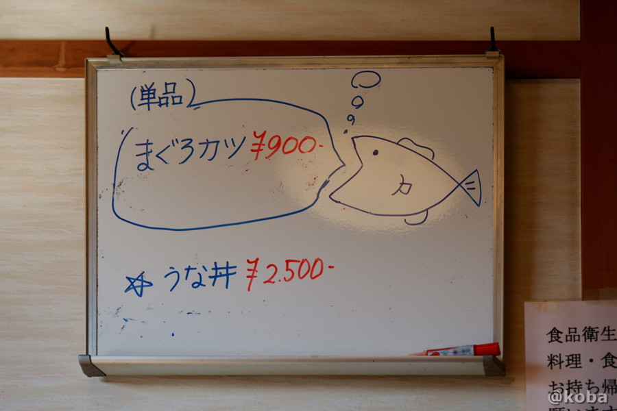かわいい魚の絵と単品メニューが書かれた、壁にかけられたホワイトボード