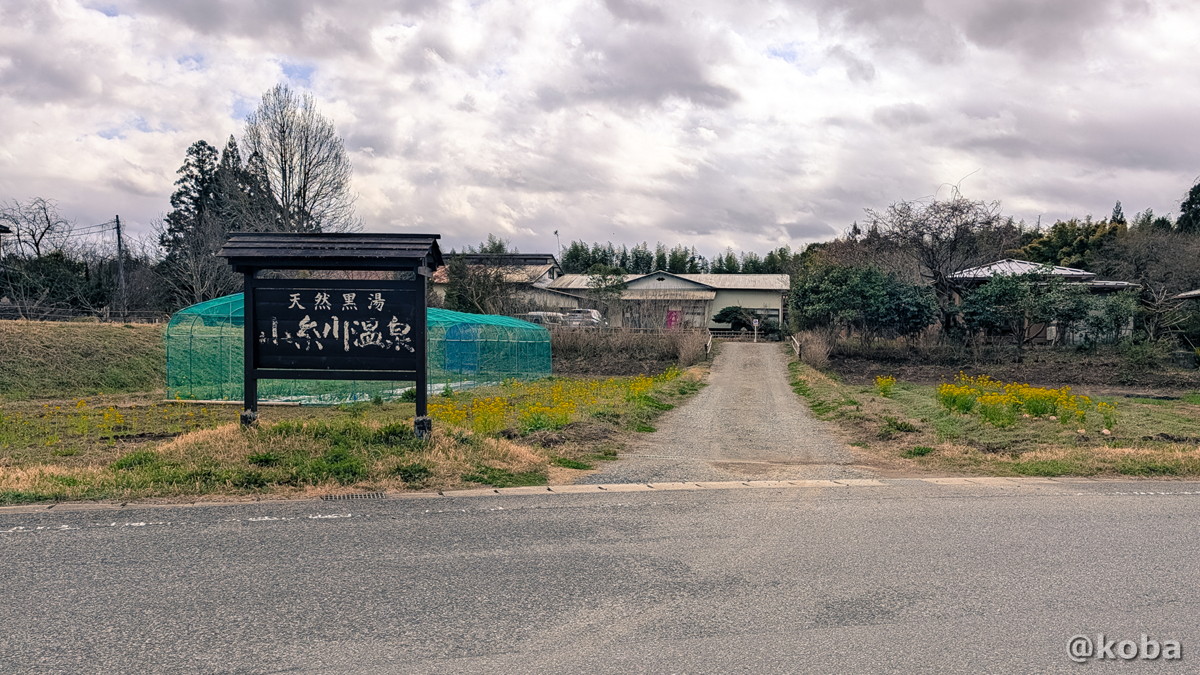 千葉県君津市にある「小糸川温泉」の道路沿いのアプローチ。古い看板には「天然黒湯」の文字が書かれている。