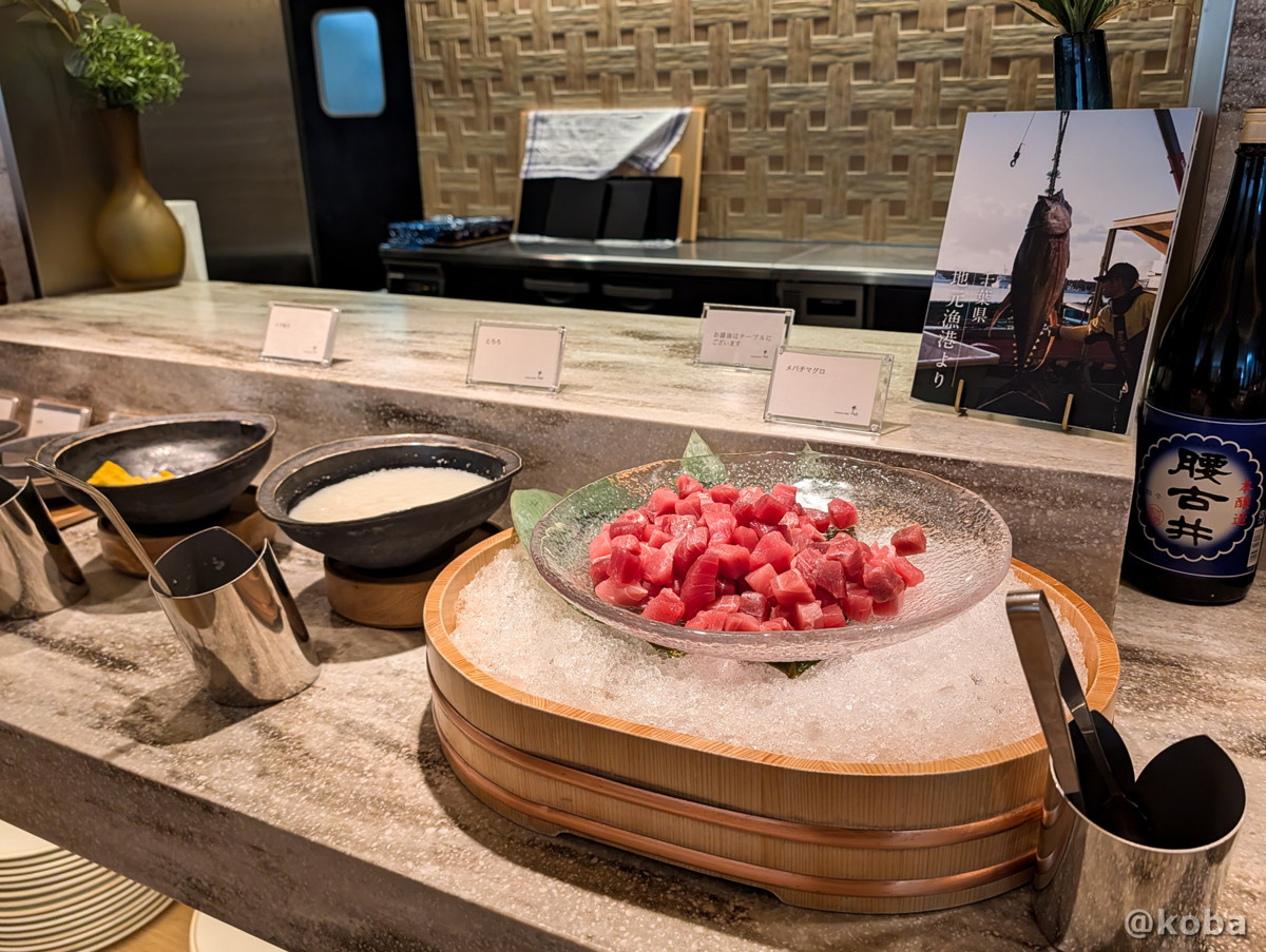 ホテルハーヴェスト勝浦の朝食ビュッフェ。氷で冷やされた透明な器に入ったマグロのぶつ切りと、とろろや卵焼きなどが並ぶ山かけコーナーの写真。