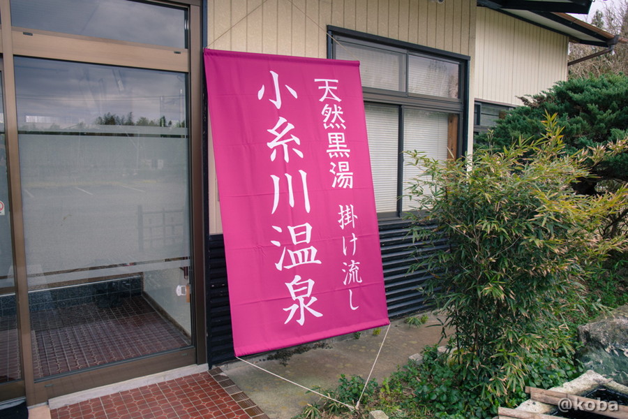小糸川温泉の玄関横に下がっている、「小糸川温泉 天然黒湯 掛け流し」と書かれた垂れ幕のクローズアップ写真。