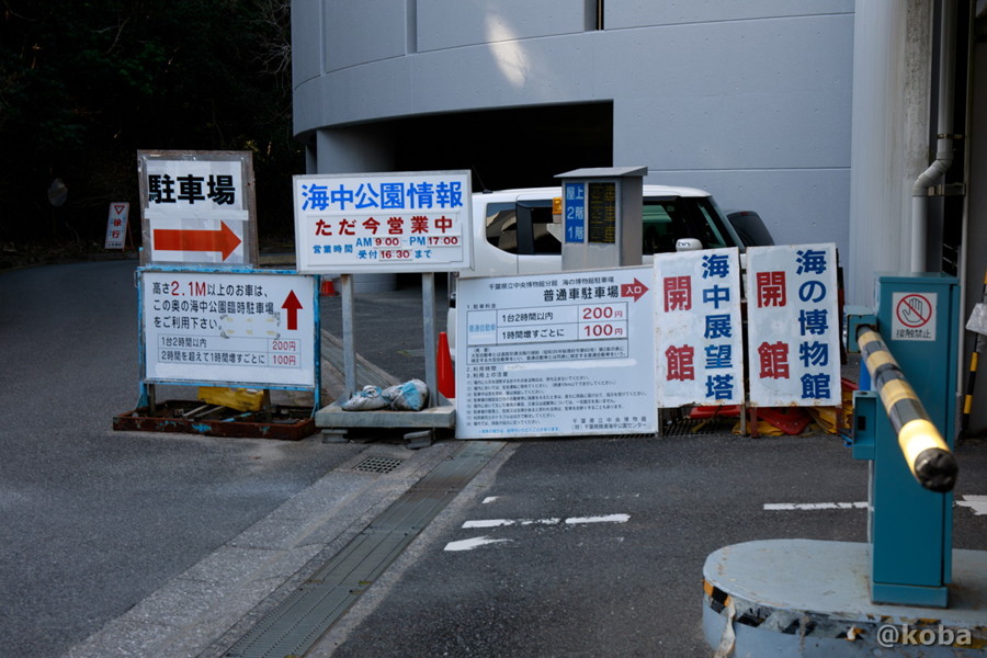 千葉県勝浦市「海の博物館」の駐車場入り口と、利用料金などが書かれた案内看板の写真。