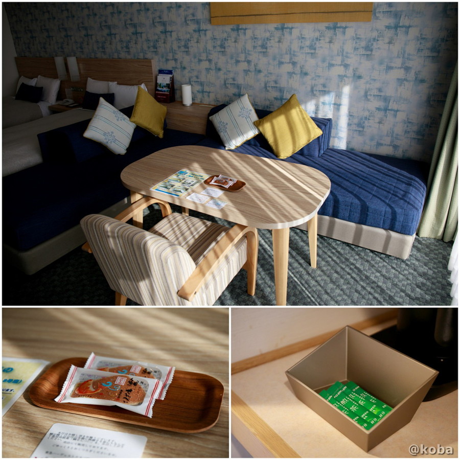 ホテルハーヴェスト勝浦の客室にある、お茶請けの鯛せんべいと伊藤園の粉末茶が置かれたテーブルと、ベッドにもなるソファの写真。