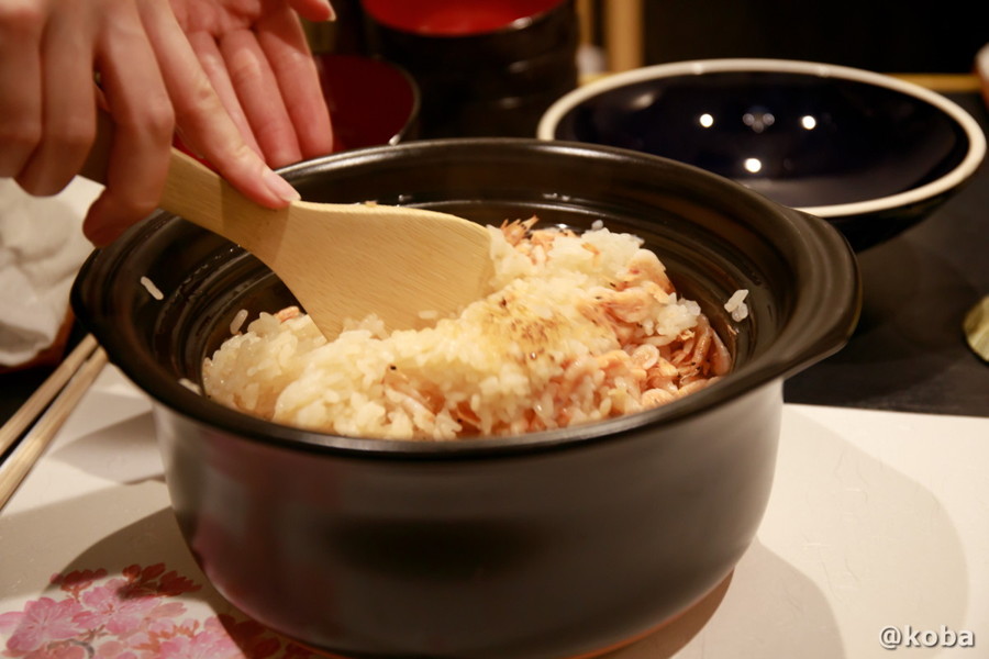 和心うららかの食事、土鍋で炊き上げられた「桜エビの炊き込みご飯」を店員さんがしゃもじでかき混ぜている写真。