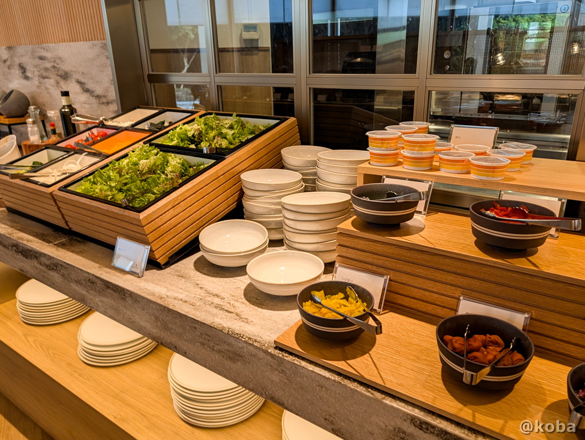 ホテルハーヴェスト勝浦の朝食ビュッフェ。納豆やお漬物、色とりどりの新鮮な野菜と多彩なドレッシングが並ぶカウンターの写真。