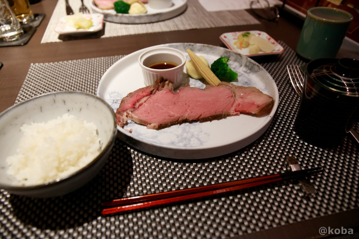 ホテルハーヴェスト勝浦の夕食のメインである、グレイビーソースがかかったローストビーフと、白米、赤出汁、香の物の食事セットの写真。