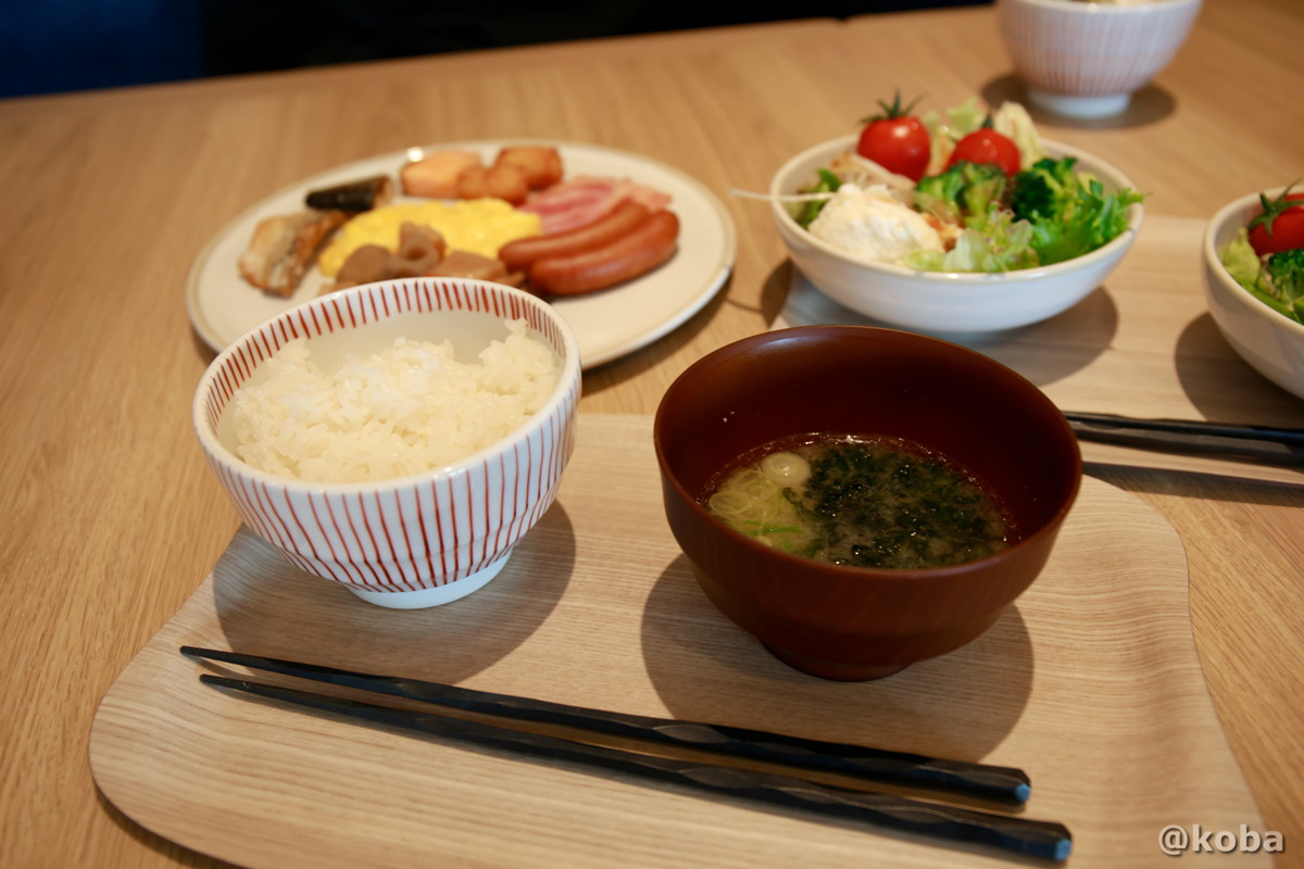 ホテルハーヴェスト勝浦の朝食ビュッフェで、ご飯、お味噌汁、サラダ、焼き魚などのおかずを盛り付けてテーブルに並べた全体写真。