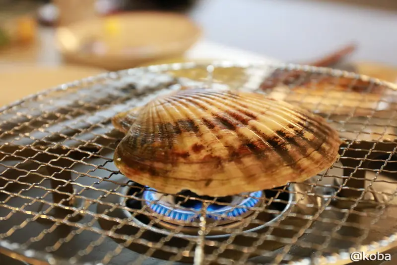 コンロの火にかけられ網の上で少しずつ口が開き始めたホタテ
